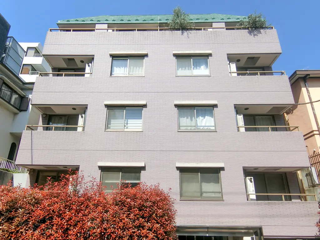 現代的な外観のアパートビル、ベランダ付き、赤く紅葉する植木と青空
