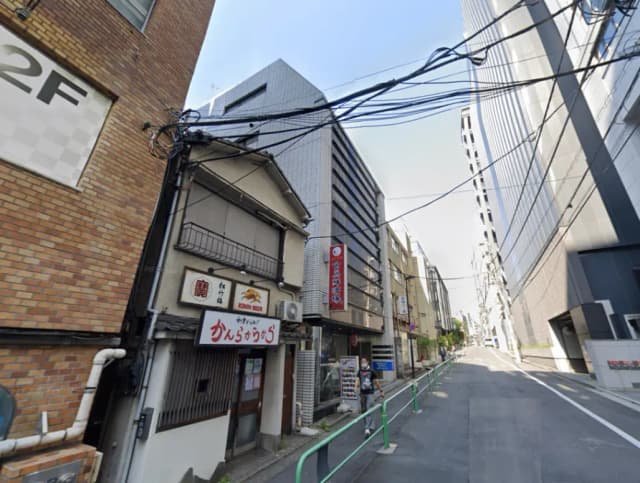 - 都市の静かな通り、古い和風の飲食店が隣接し、高層ビル群が立ち並ぶ街並みの風景