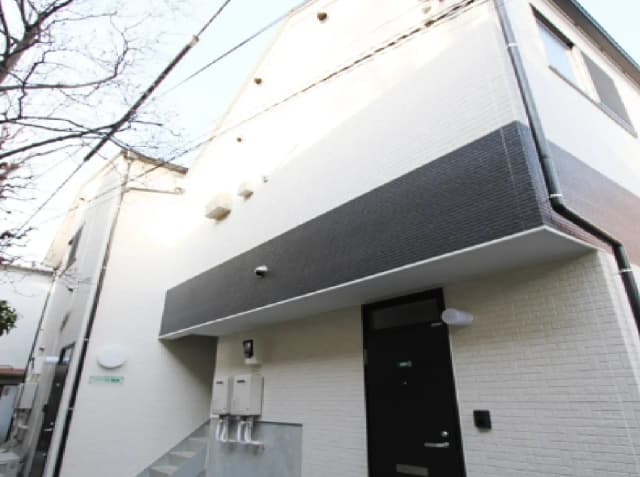 - 白と黒のシンプルな外壁デザインの建物、階段とエントランス、周囲に細い電線が見える外観