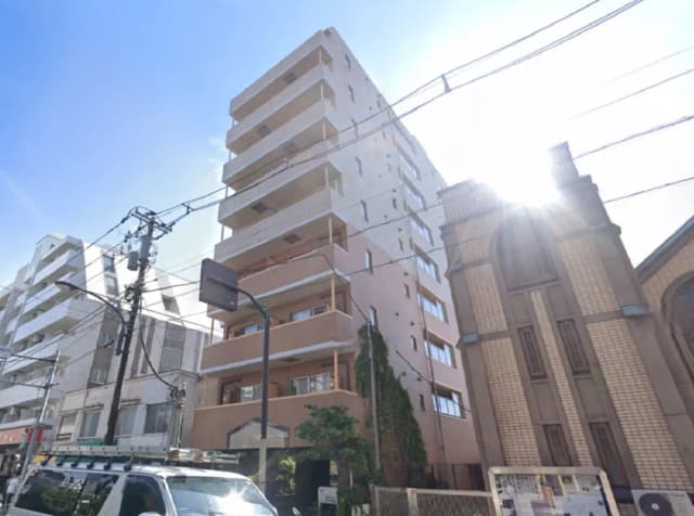 周辺に高層ビルが立ち並ぶ街並みの中にある、モダンなデザインの6階建てマンションの外観、隣には歴史的な建物が見える景観