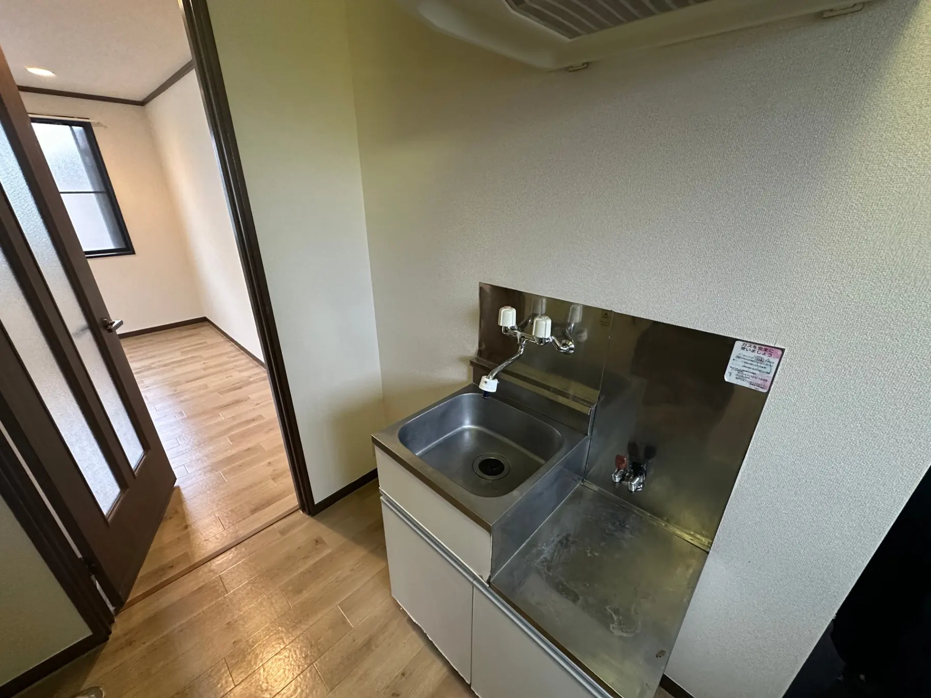 シンプルなデザインの洗面台と木製フローリング、白い壁の明るい空間