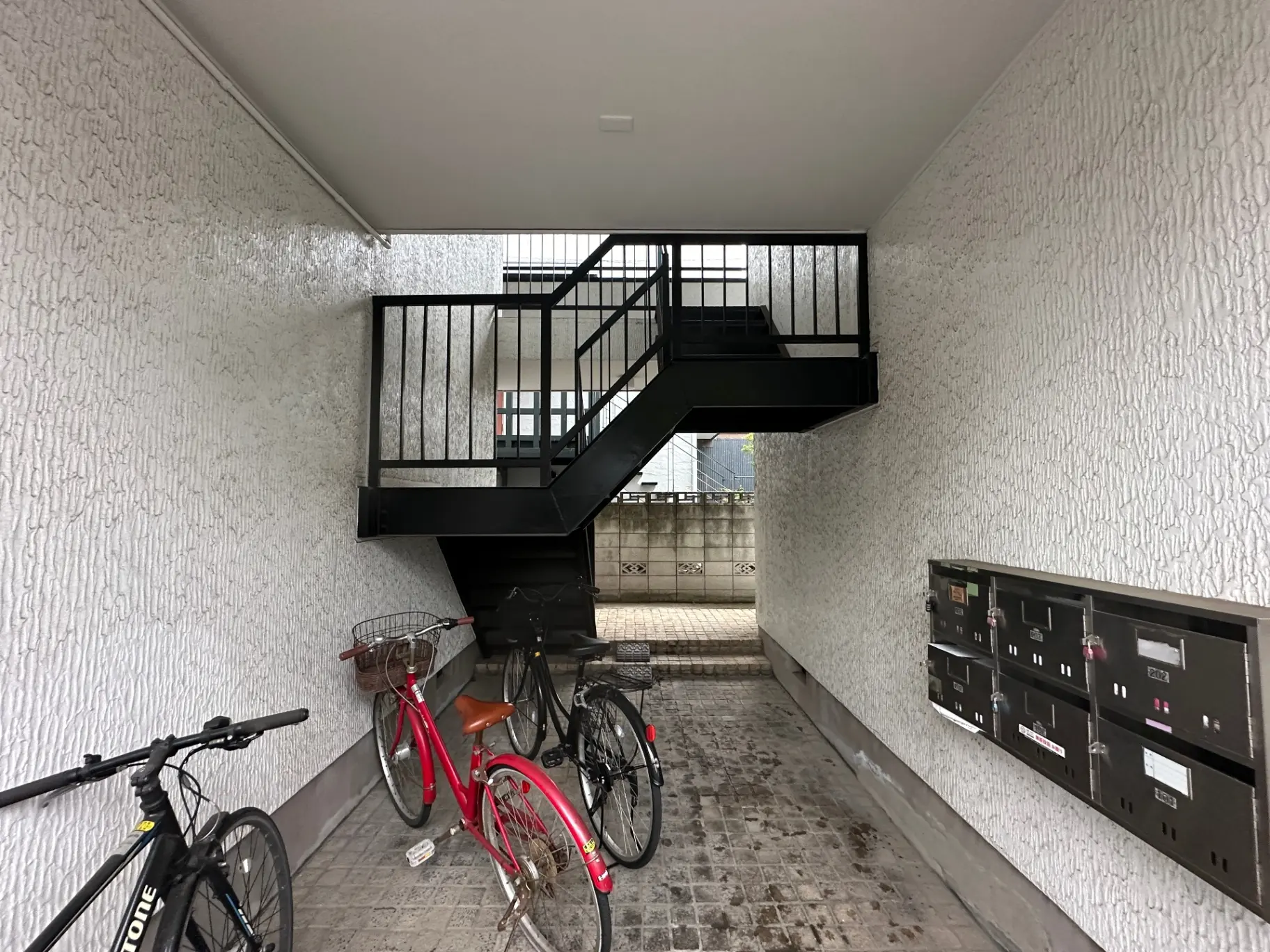 建物の入り口にある黒い鉄製の階段と壁に設置された郵便受け、自転車が並んでいる風景