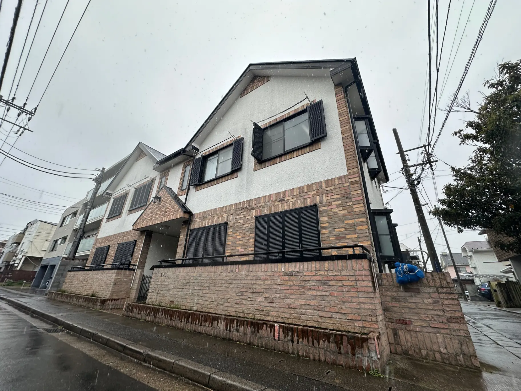 雨の日の都市住宅、赤レンガの外壁と黒いシャッターが特徴的なモダンな家の外観