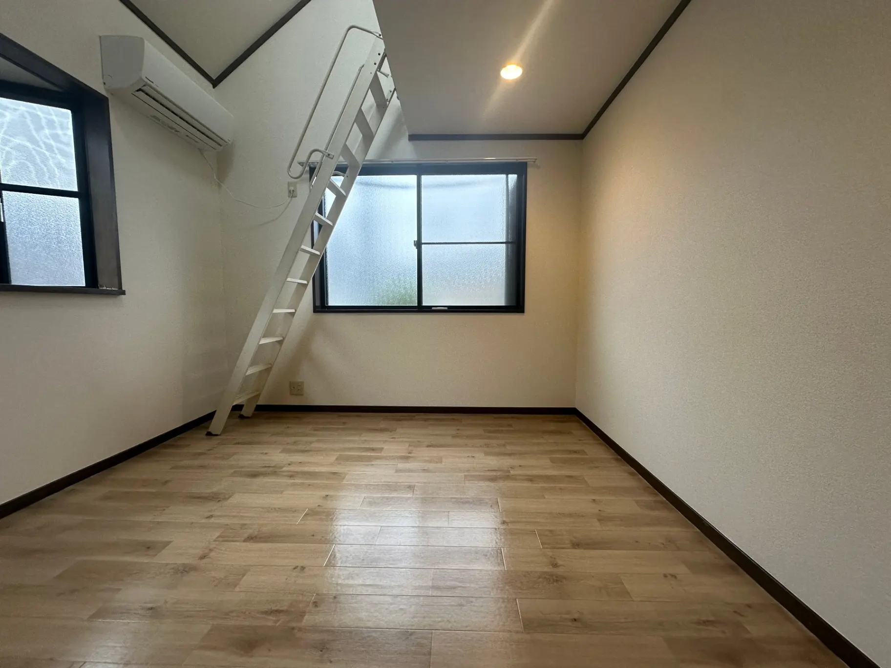 シンプルで広いリビングスペース、木目調のフローリング、白い壁、階段付きの屋根裏部屋