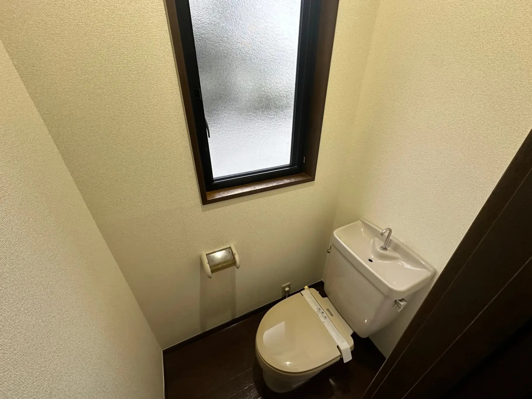 コンパクトなトイレルーム、壁に取り付けられた手洗い器、小窓からの採光