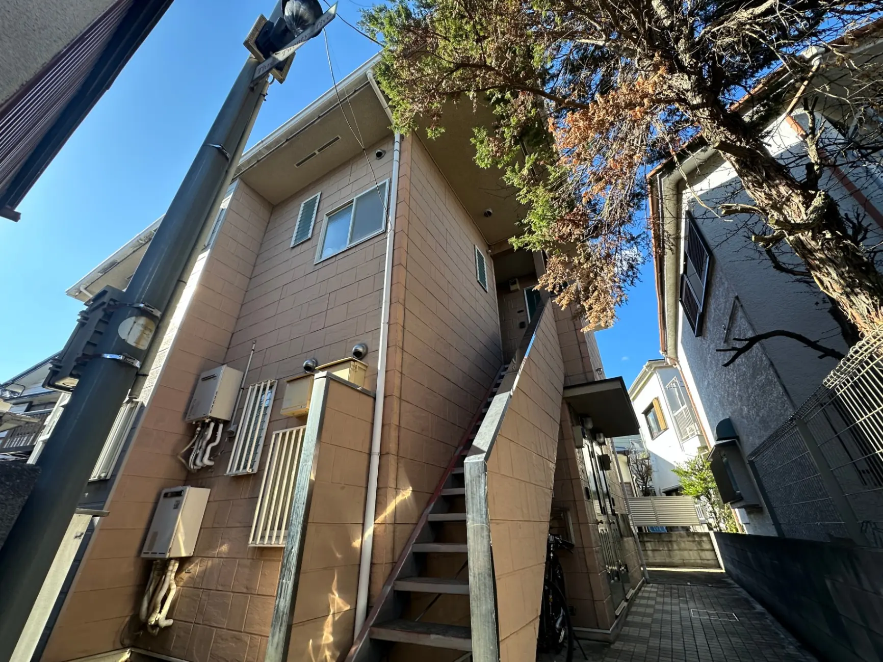 日本の住宅街にあるベージュの外壁のアパート、晴天の下での階段と自転車置き場