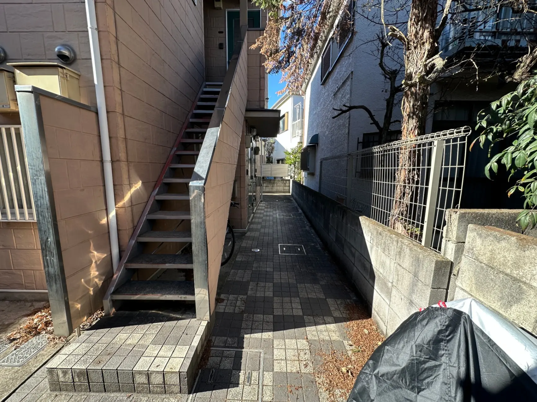 都市の住宅街の狭い通路、階段とフェンス、建物の壁に沿った影が映る外観