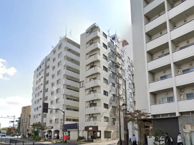 - 都市部に立つ高層マンション群、隣接する商業施設や公道が見える風景、青空と雲が広がる景観