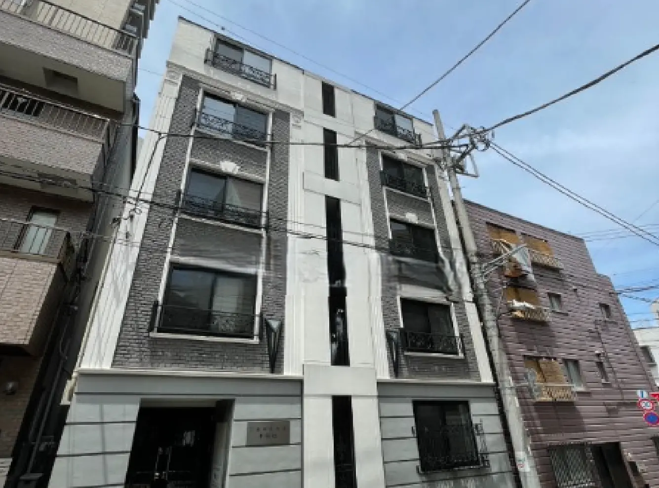 - シンプルでモダンなデザインの住宅ビル、グレーの外壁と大きな窓が特徴、隣接する建物とのコントラストが際立つ外観