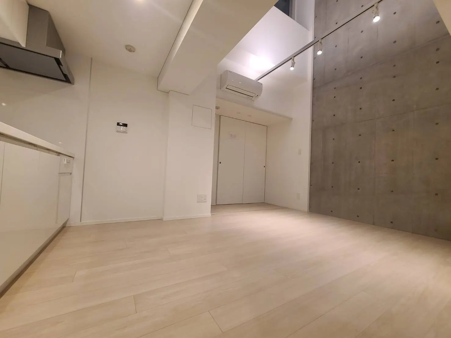 ミニマルデザインの広々としたリビングルーム、コンクリートのアクセント壁、白い壁、木目調の床、天井にレール照明