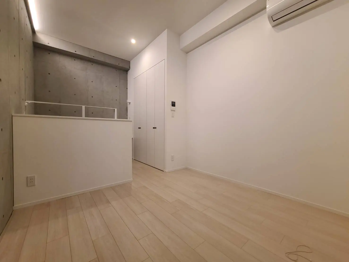 シンプルモダンな内装の部屋、コンクリート壁と木目調フローリング、白いドアとエアコンのあるインテリア