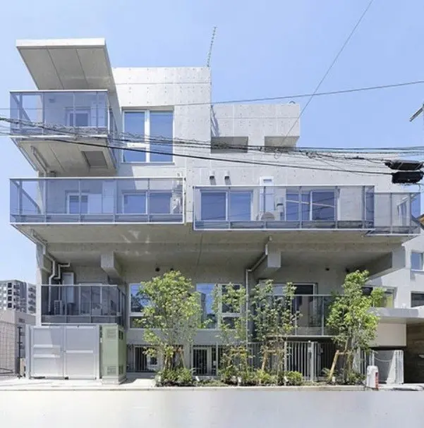 現代的なデザインのコンクリート住宅、ガラスのバルコニーと新緑の植栽が特徴の外観