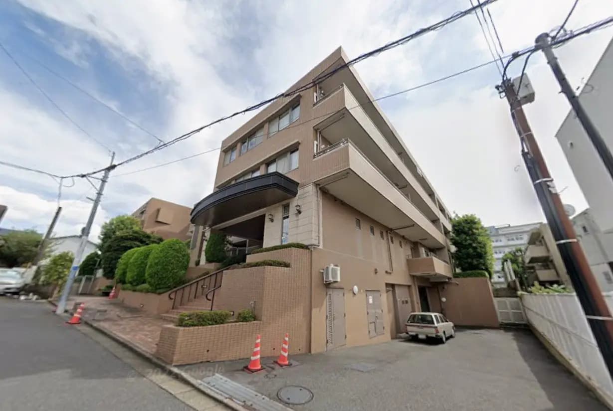 都市部に位置するベージュ色のマンション外観、くぼみのあるバルコニーと緑豊かな装飾が特徴