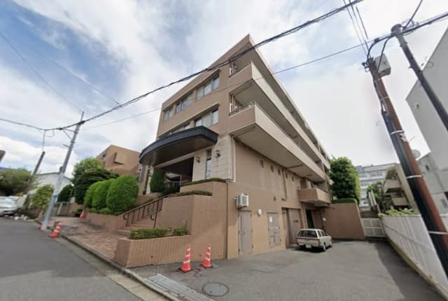 都市部に位置するベージュ色のマンション外観、くぼみのあるバルコニーと緑豊かな装飾が特徴