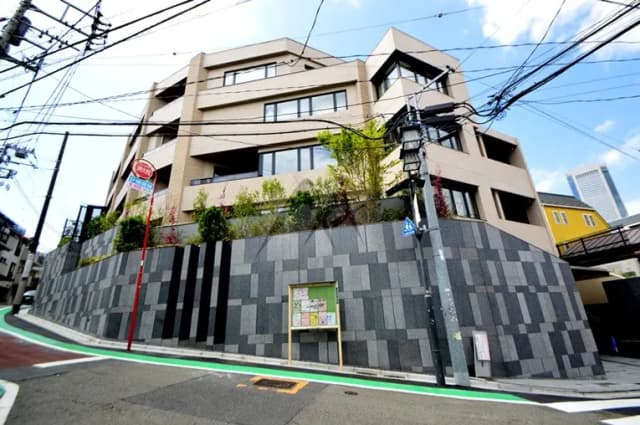 街角にある現代的な外観の都市型マンション、植栽付きの壁とクリアな青空