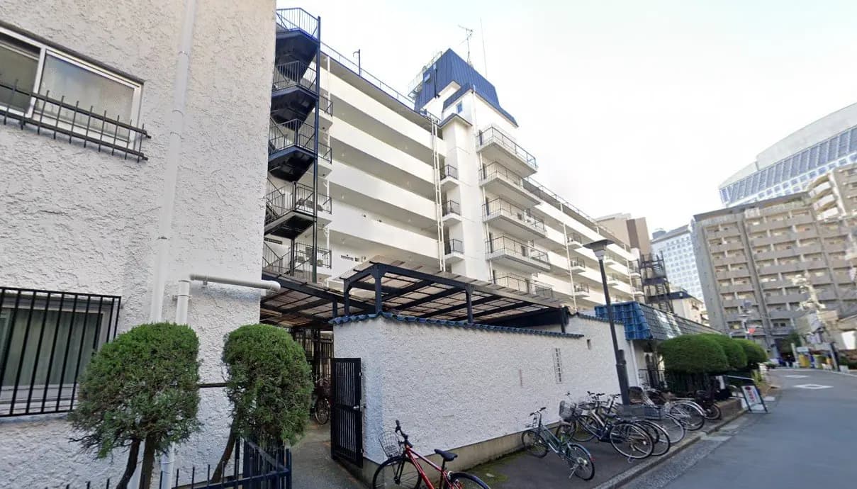 都会の住宅街に位置する白い壁のマンション、自転車駐輪スペースあり