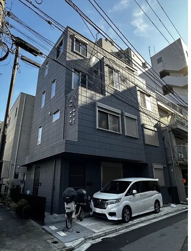 都市の住宅街にあるモダンな外観のアパートメントビル、駐車場には白い車