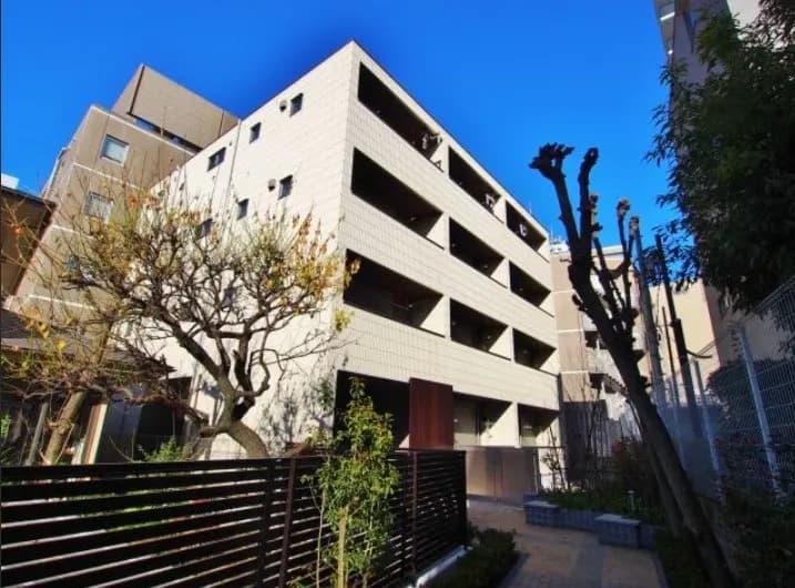 モダンな外観の都市型マンション、晴天の下での青空、樹木とフェンスが映えるシーン