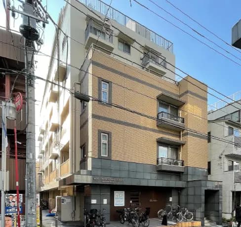 市街地に建つ現代的な外観のアパートビル、晴天の下、電柱と自転車置き場が見える街角