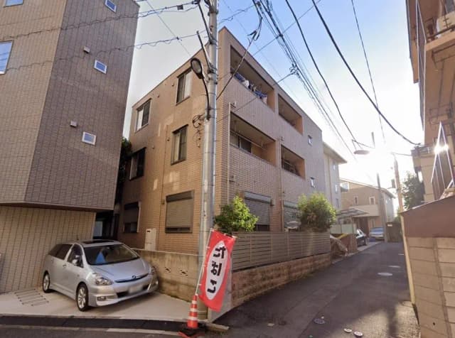 日本の閑静な住宅街、茶色のアパートビルと駐車中のシルバーの車、路地と電線が見える風景