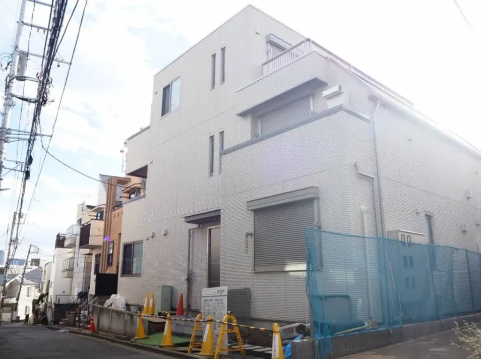 都市の住宅街にある現代的な白い外壁の家、電線が通る通りの風景