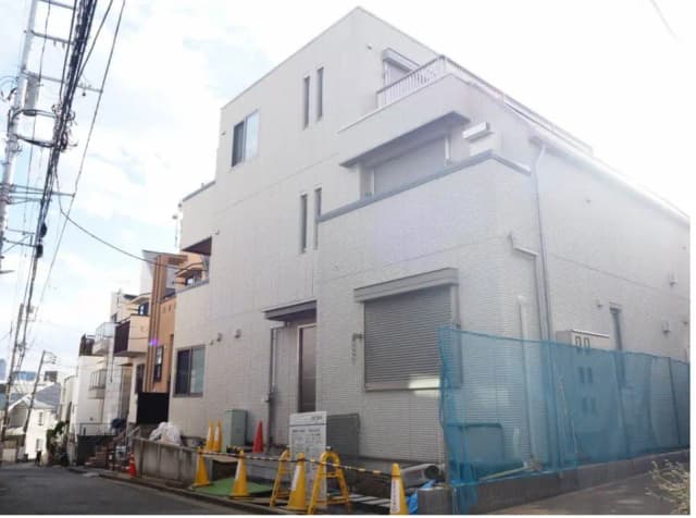 都市の住宅街にある現代的な白い外壁の家、電線が通る通りの風景