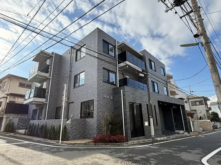 現代的な外観の新築マンション、グレーのタイル壁、ガラスのバルコニー、晴れた日の市街地景観