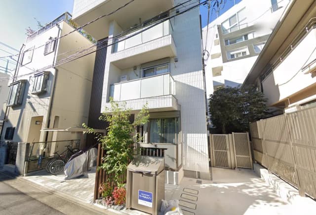 日本の都市部にあるモダンな住宅、白とベージュの外壁、バルコニー付き、自転車が置かれたエントランス