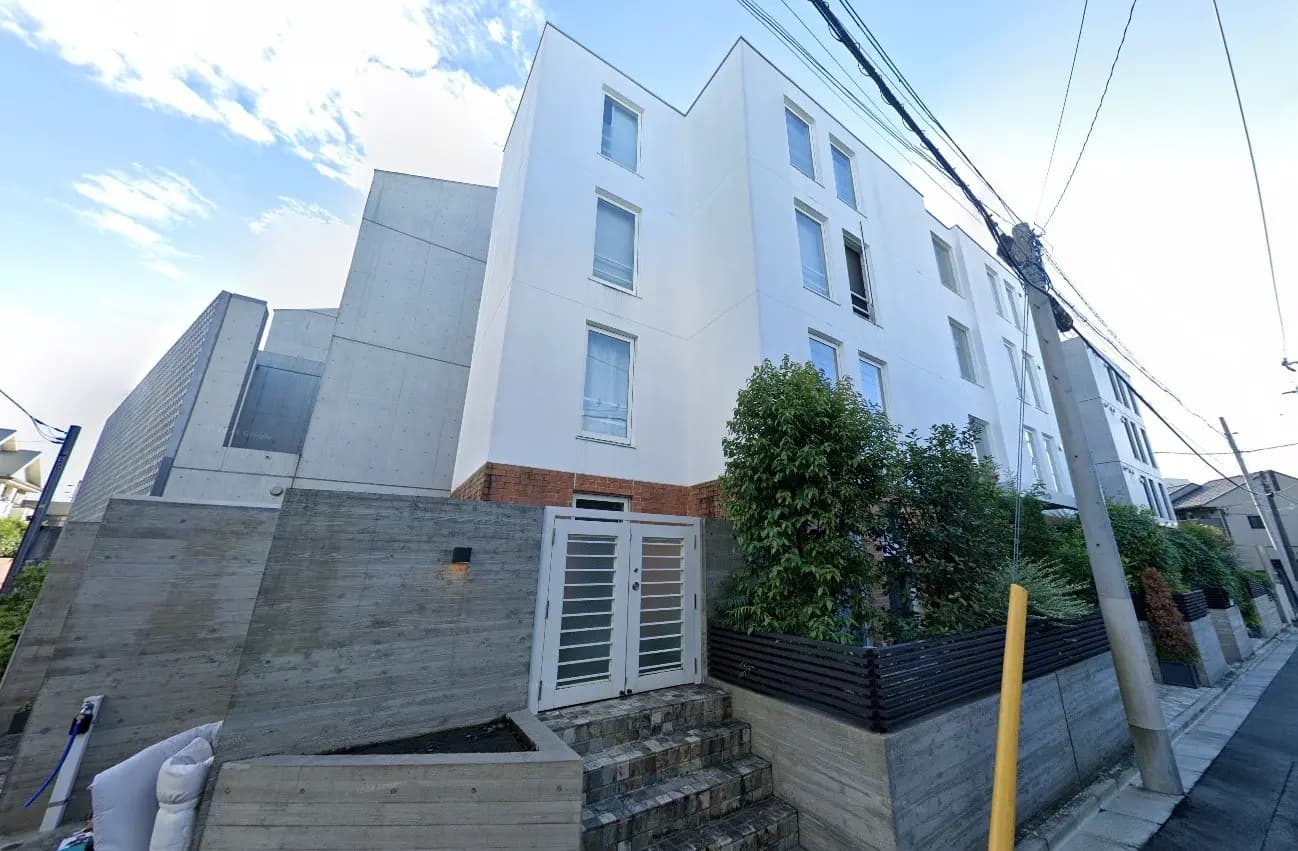 - モダンなデザインの多棟住宅、白い外壁と庭に囲まれたエントランス、緑豊かな植栽が施された外観