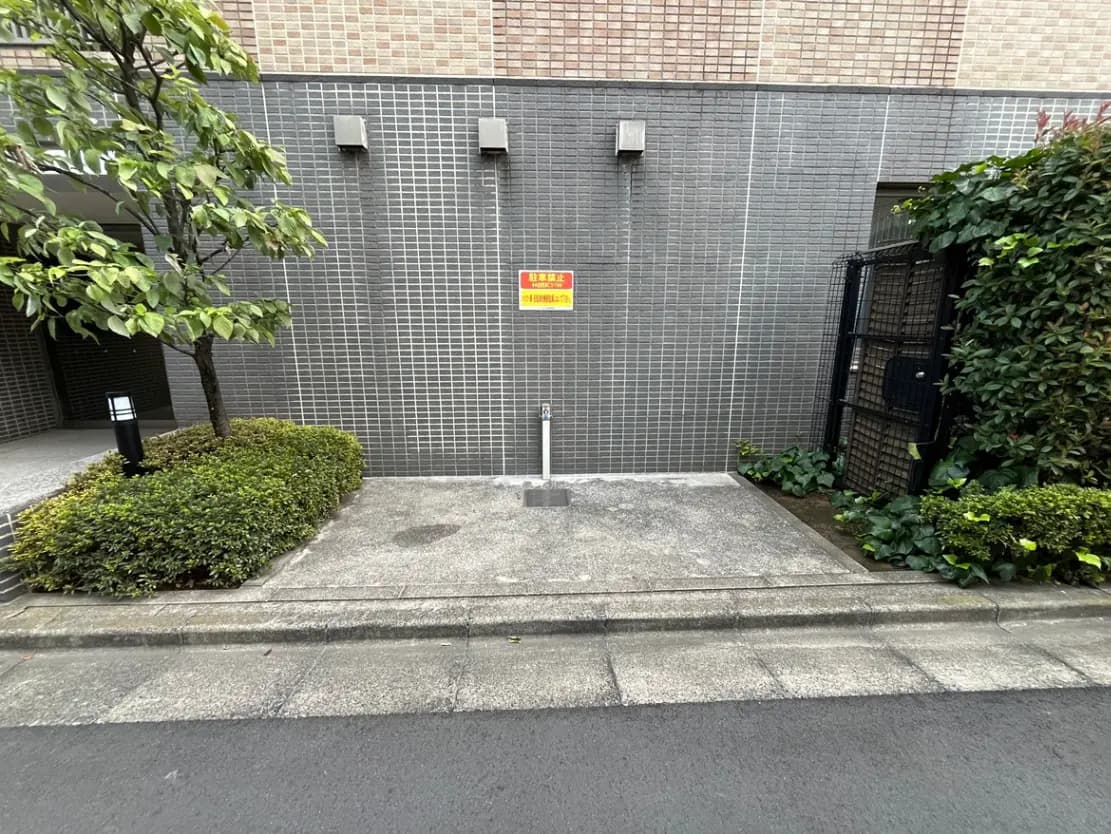 - モダンな外壁と緑の植栽、消火栓と照明が配置されたマンションのエントランス周辺の風景