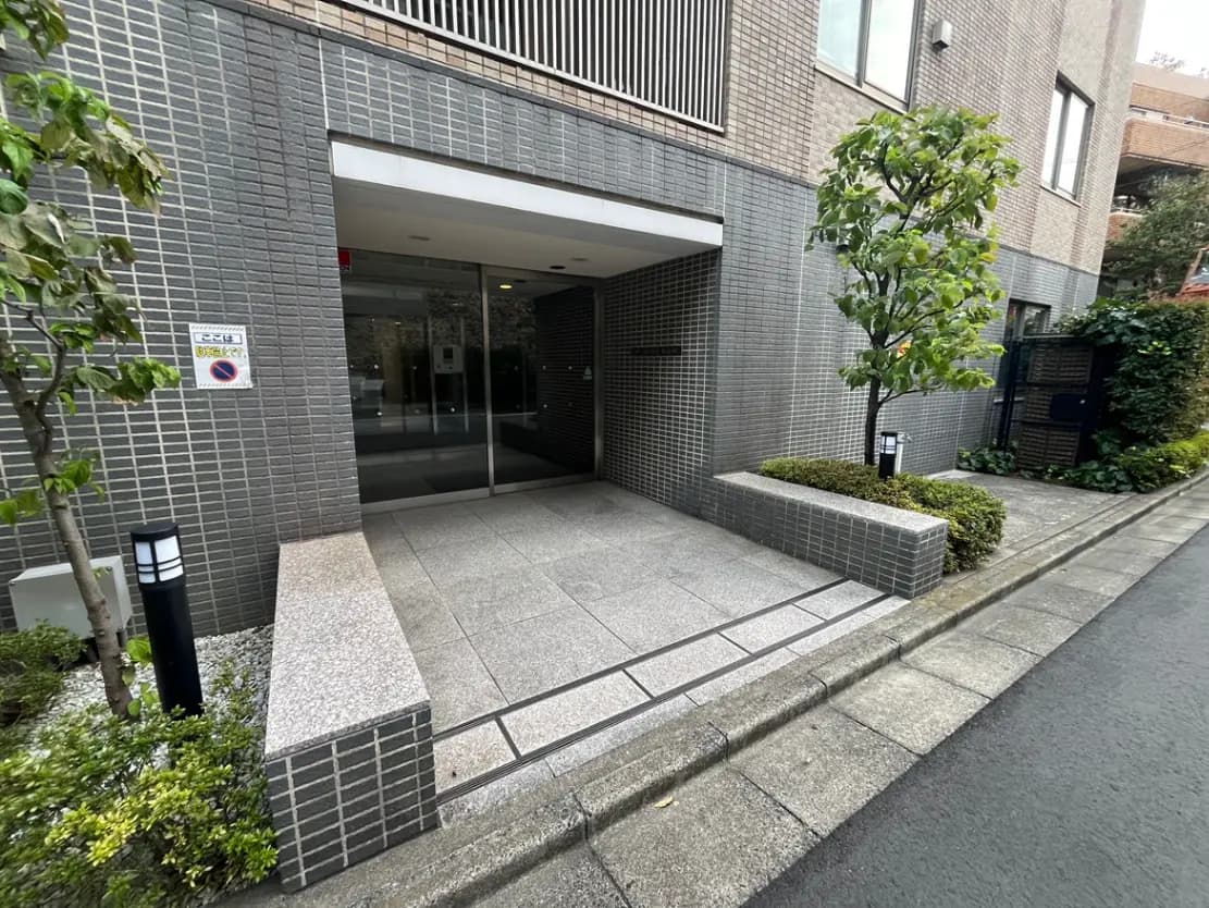 - モダンなデザインのエントランス、グレーのタイルの壁、植え込みと照明が整ったアプローチの風景