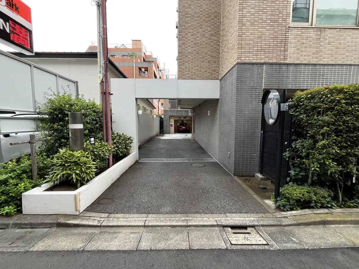 - 明るい日射しの中、小道に続くマンションの入り口、緑豊かな植栽と洗練された外観の写真