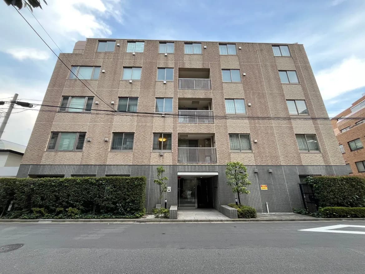 - モダンな外観の集合住宅、ブラウンのタイル張り、緑の植栽があるエントランスと四階建てのビルの景観