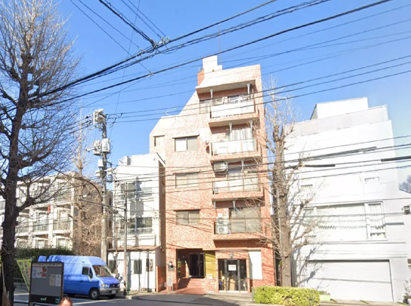 - 複数の建物が並ぶ通りの風景、レンガ造りのマンションと青い空、電線が張り巡らされた都市の一角
