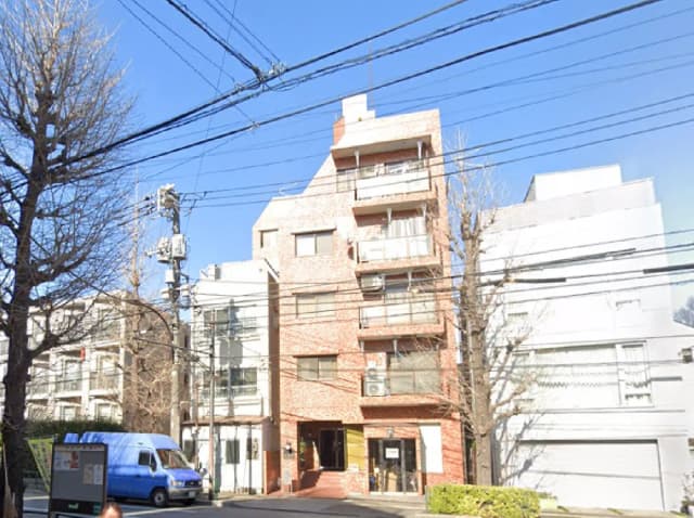 - 複数の建物が並ぶ通りの風景、レンガ造りのマンションと青い空、電線が張り巡らされた都市の一角