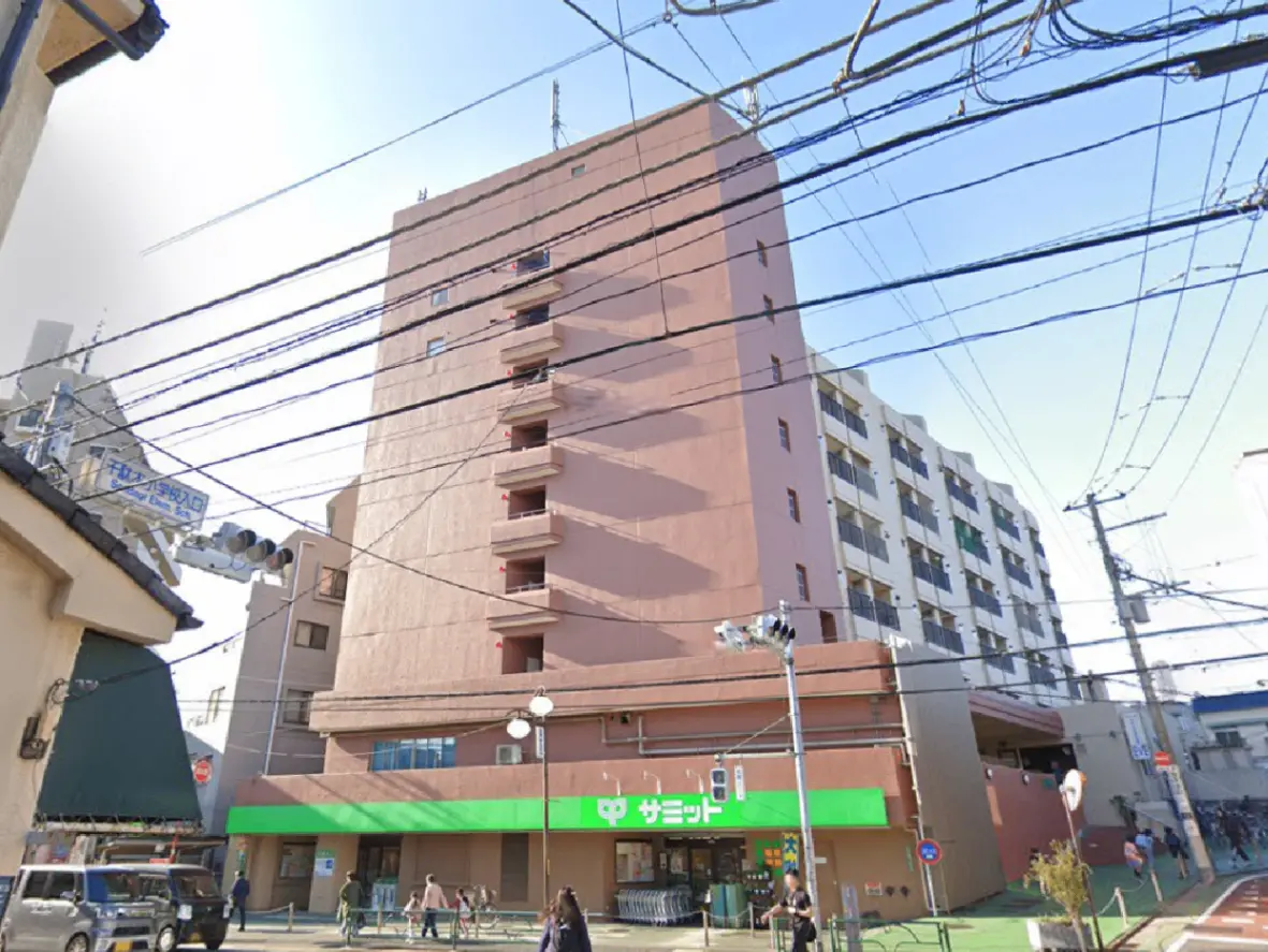 - 商業施設とマンションが並ぶ都市の風景、電線が交錯する通りの様子