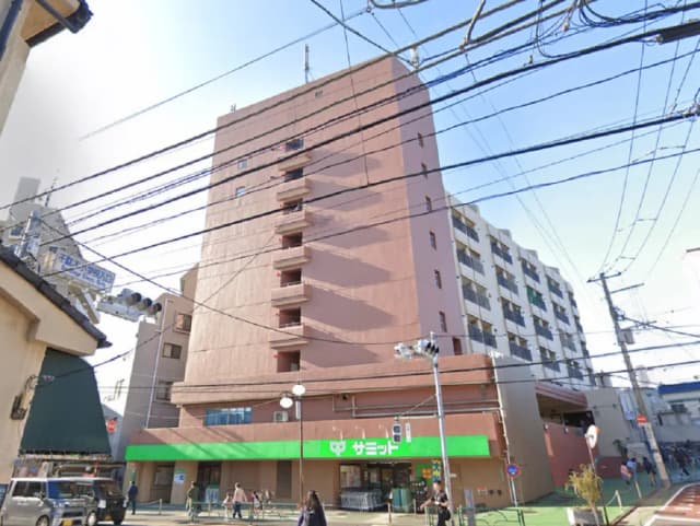 - 商業施設とマンションが並ぶ都市の風景、電線が交錯する通りの様子