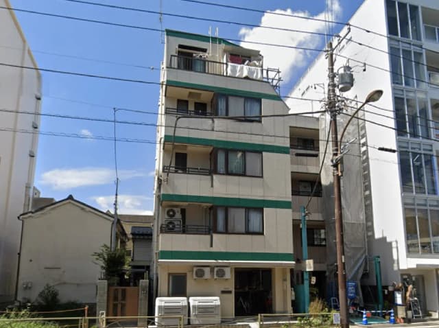 - 緑のアクセントが特徴的な4階建てのアパートの外観、隣接するビルと青空が広がる風景
