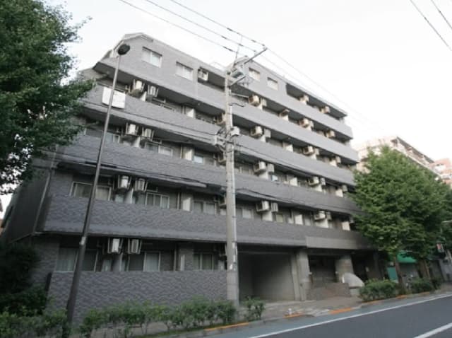 - グレーの外観を持つ5階建てのアパートメントビル、周囲には緑の木々と街路灯、エアコンが設置された窓が目立つ外観