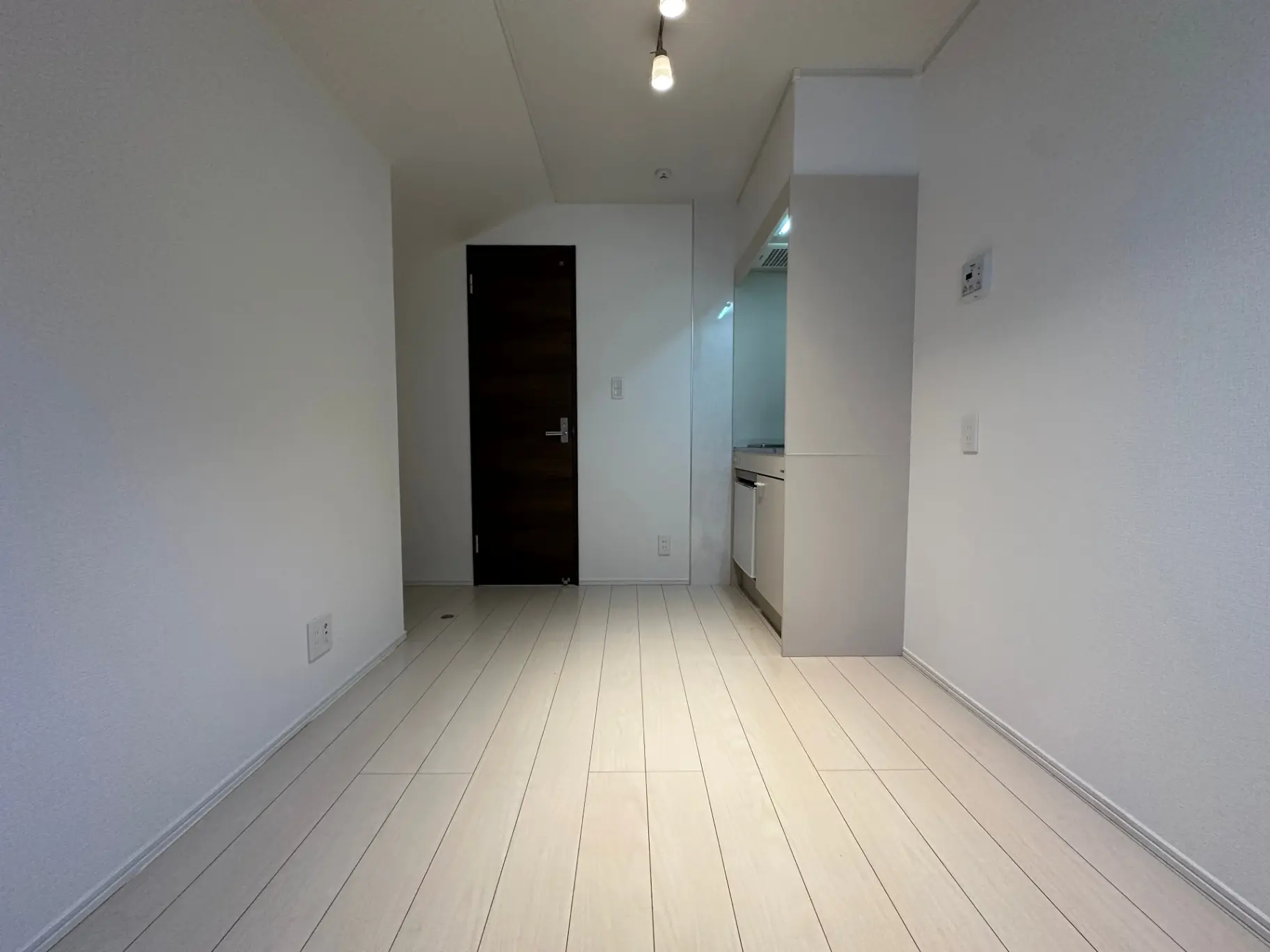 シンプルで清潔なデザインの空の部屋、白い壁と木目調のフローリング、天井ライトの明るい照明