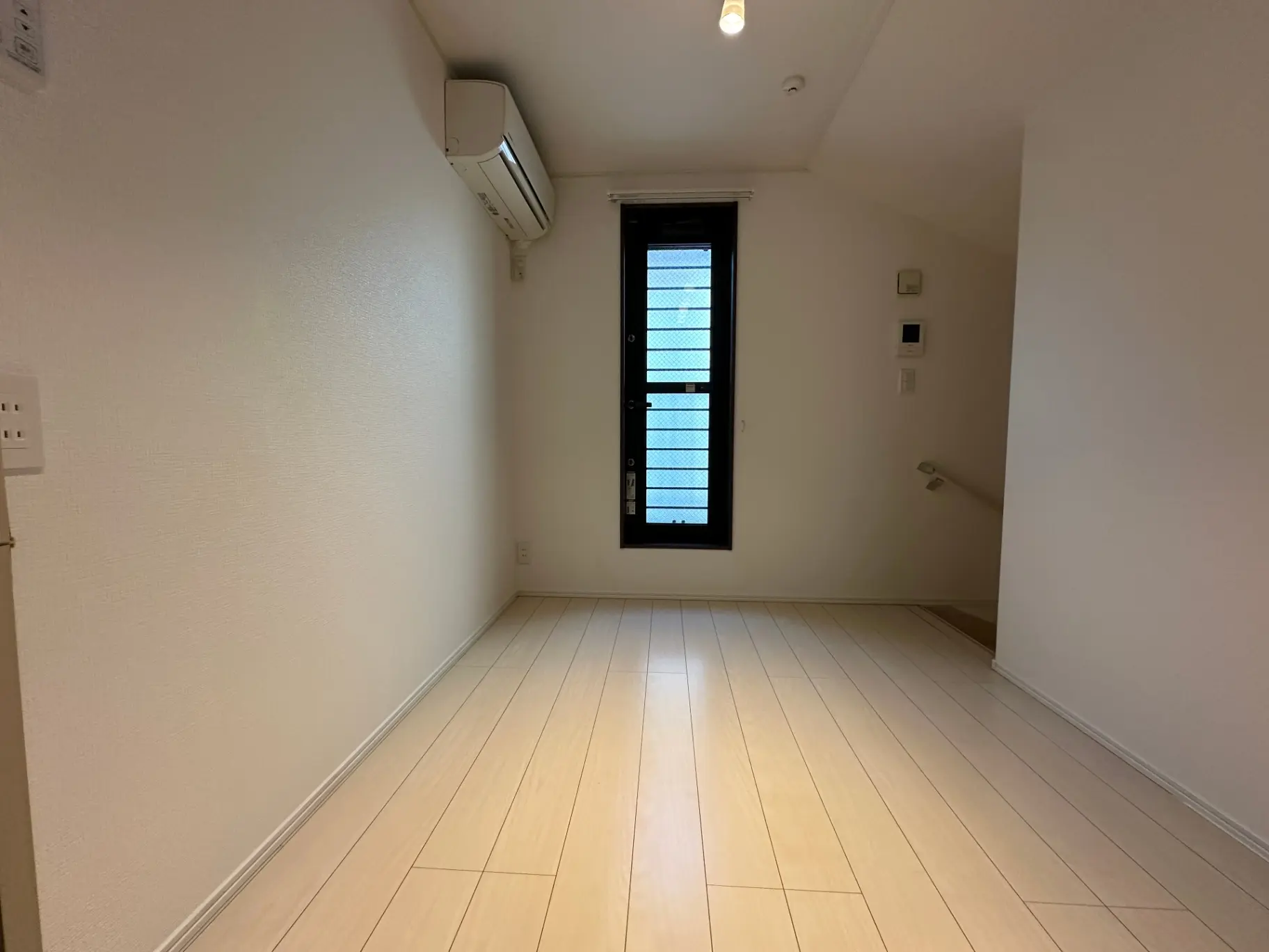 シンプルなデザインの空き部屋、白い壁と木製フローリング、エアコンと小さな窓のあるインテリア