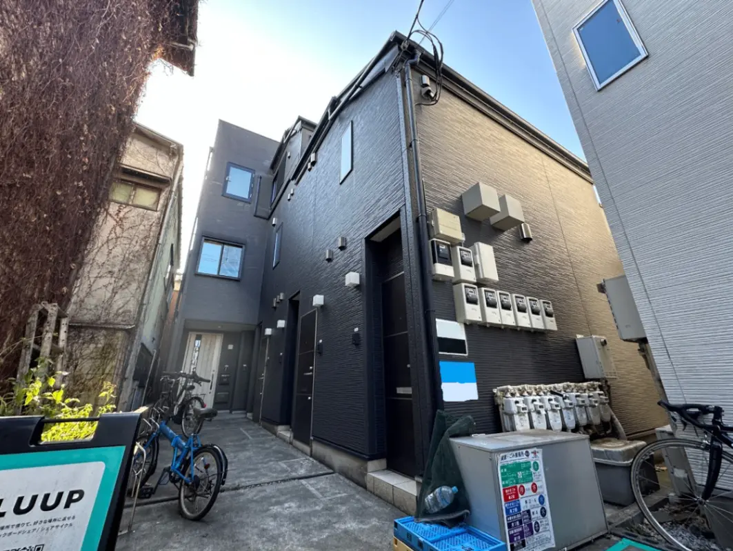 日本の都市風景、狭い路地に並ぶ現代的な建物と自転車、エアコン外部機と電力メーターが壁に取り付けられたアパートの外観