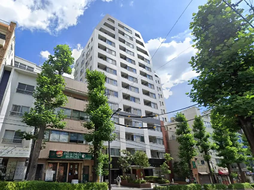 - 現代的な外観のマンション、周囲に緑の木々が立ち並び、青空と雲が広がる街並みの風景