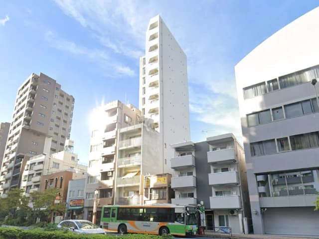 - 都市の風景、様々な高さのビルが立ち並ぶ中、中央に白い高層ビルと緑色のバスが見える街並み