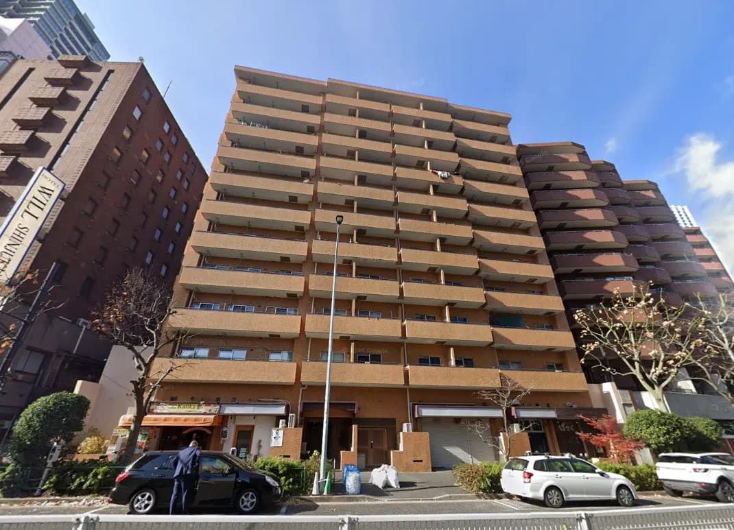 - 都市型マンションの外観、7階建てのレンガ調のファサード、隣接する建物と青空の下の景観