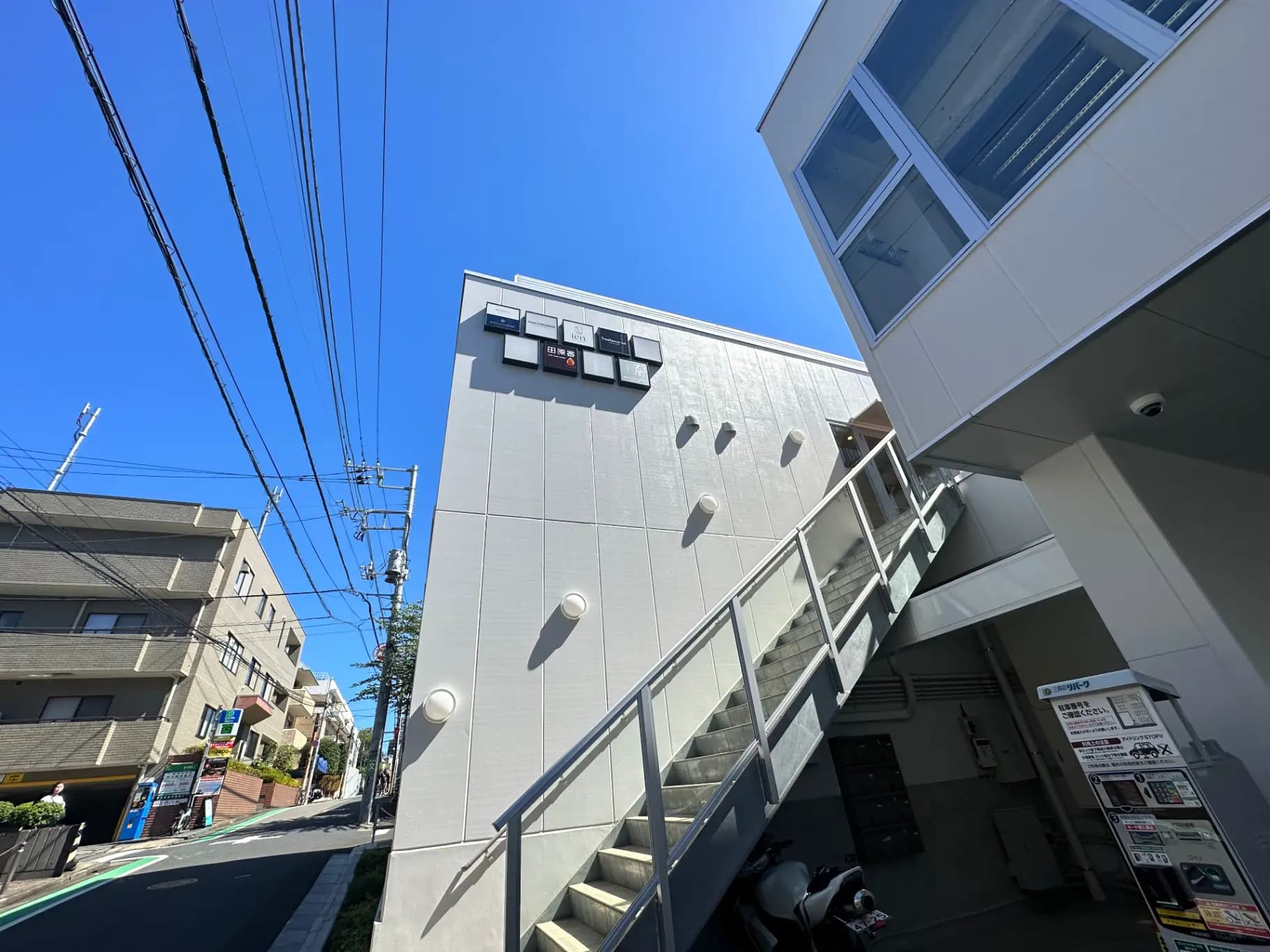 日本の住宅街にある現代的な建築デザインのアパート、青空と電信柱が見える景色
