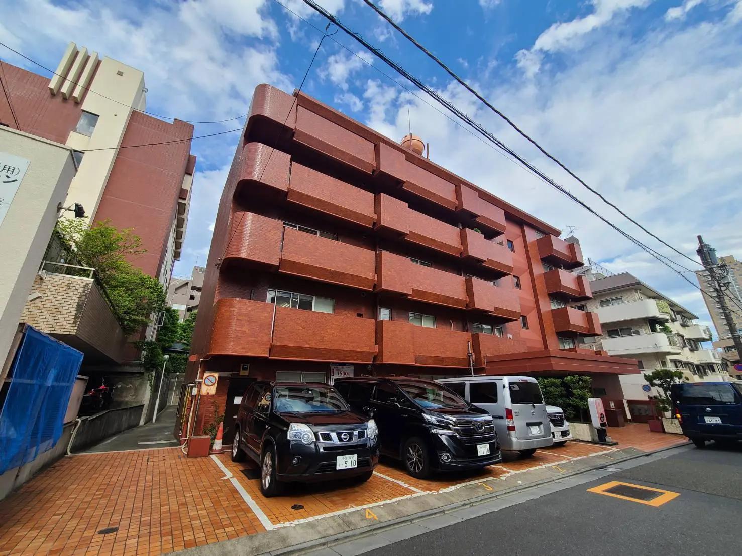 赤茶色の外壁と駐車場を備えた都市型マンション、青空と電線が見える景観