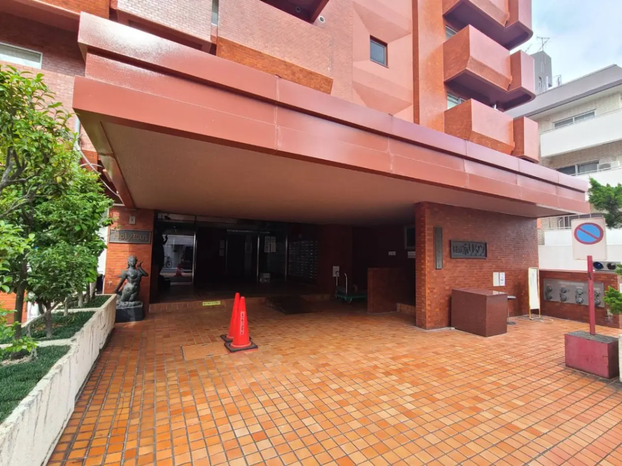 レンガ造りの外観とエントランス、植栽と看板がある建物の入口、停車禁止の道路標識