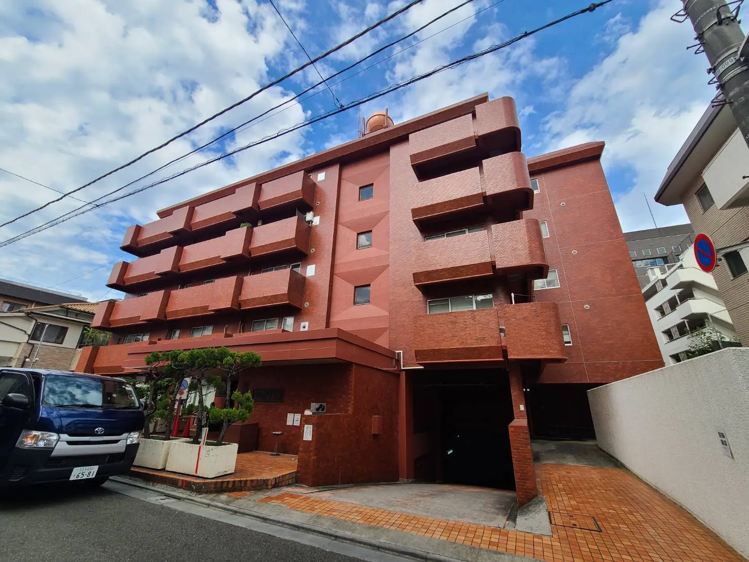 都市型のモダンなマンション、レンガ調の外観デザイン、日本の住宅街に囲まれた建物