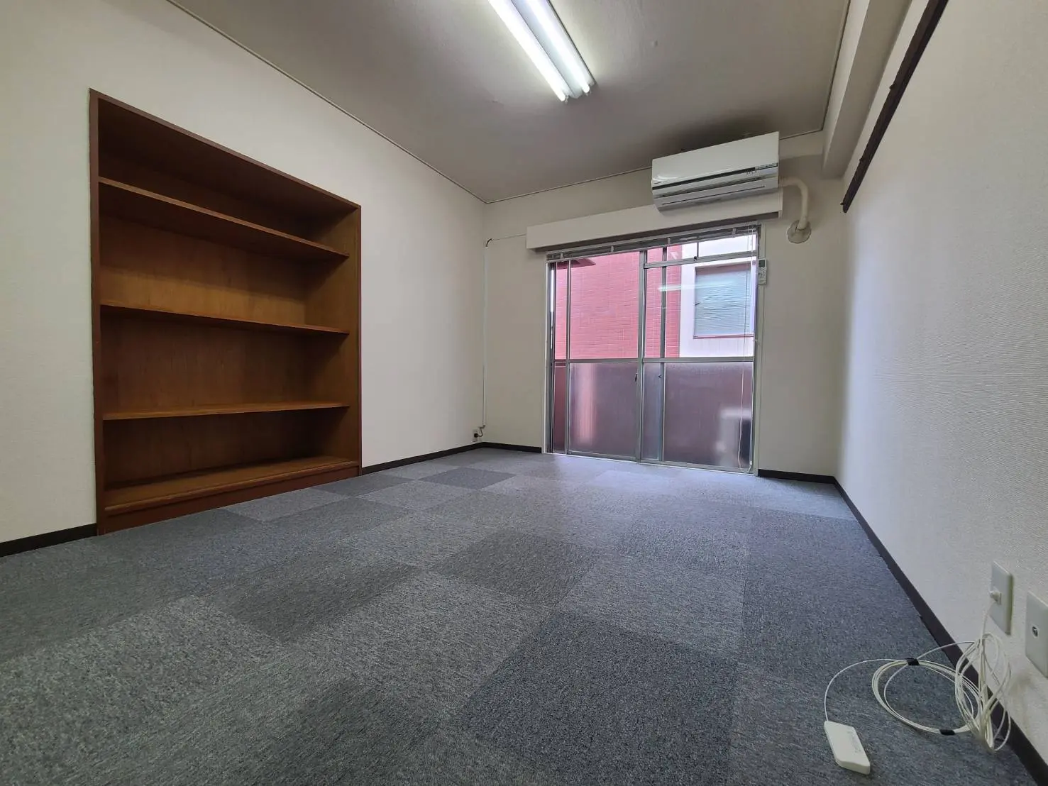 シンプルなデザインの空の部屋、木製の本棚と大きな掃き出し窓、グレーのカーペットフローリング